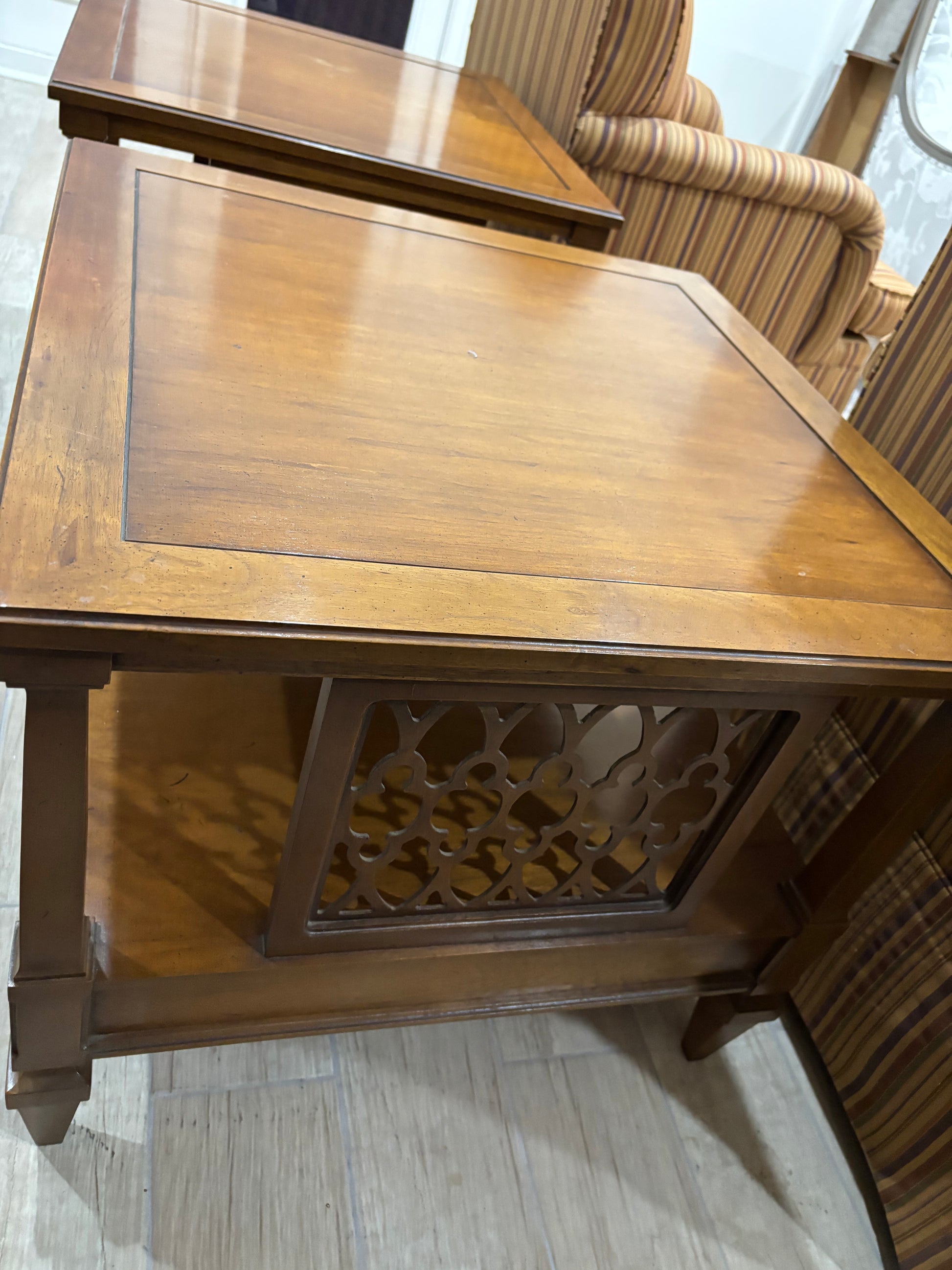 A medium brown wooden end table with a decorative carved lattice panel on the front, shown in a showroom setting.