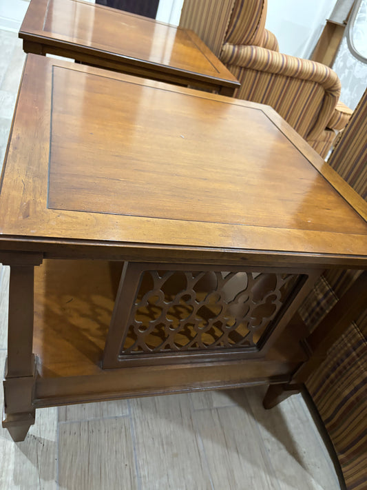 A medium brown wooden end table with a decorative carved lattice panel on the front, shown in a showroom setting.
